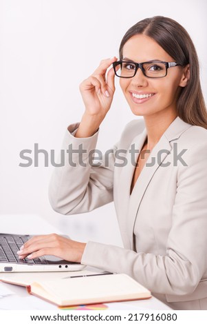 Happy businesswoman. Side view of beautiful young businesswoman holding hands clasped and smiling while sitting at her working place