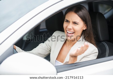 Furious driver. Angry young woman shouting and gesturing while driving a car
