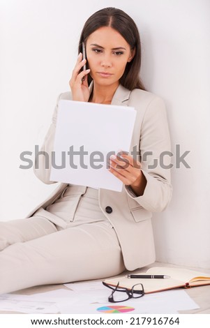 Busy working. Confident young businesswoman examining document and talking on the mobile phone while sitting on the floor