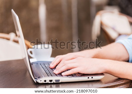 Surfing the net in cafe. Close-up of man working on laptop while sitting in sidewalk cafe