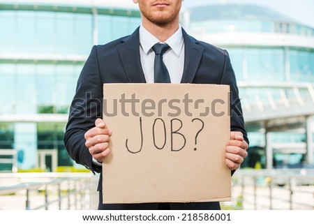 Looking for a job. Close-up of young man in formalwear holding poster with job text message while standing outdoors and against building structure