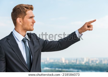 Businessman pointing away. Confident young man in formalwear pointing away while standing outdoors with cityscape in the background
