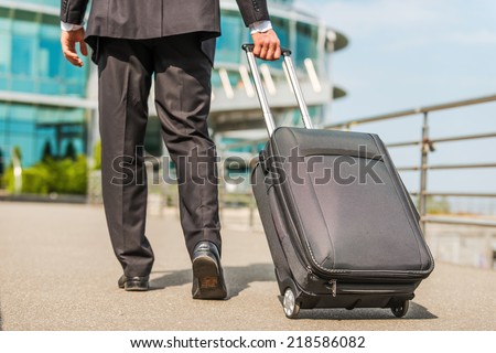 Ready to business trip. Rear view of businessman in formalwear carrying suitcase while walking away