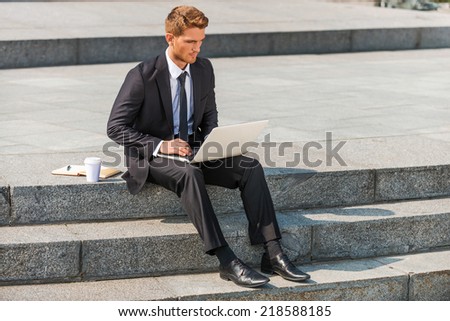Businessman working outdoors. Confident young man in shirt and tie working on laptop while sitting outdoors