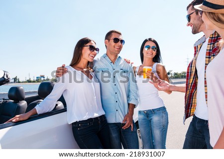 Spending great time with friends. Group of young happy people talking to each other and smiling while standing near their convertible