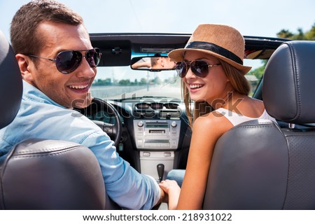 Enjoying road trip together. Beautiful young couple enjoying road trip in their convertible and looking over shoulder with smile