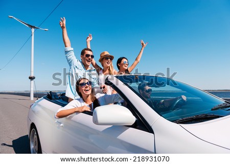 Nothing but friends and road ahead. Group of young happy people enjoying road trip in their white convertible and raising their arms up