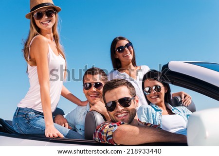 The best friends ever. Group of young happy people enjoying road trip in their white convertible