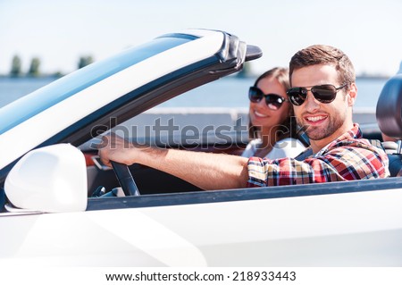 Traveling with comfort. Happy young couple enjoying road trip in their white convertible while both looking at camera and smiling
