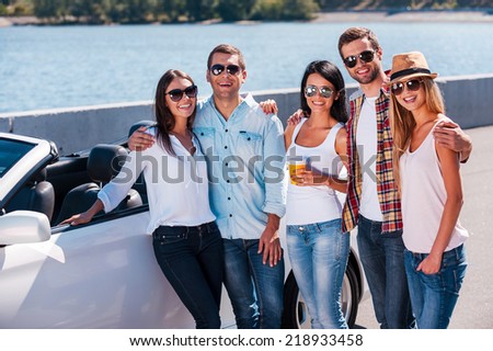 We love spending time together! Group of young happy people bonding to each other and while standing near their convertible