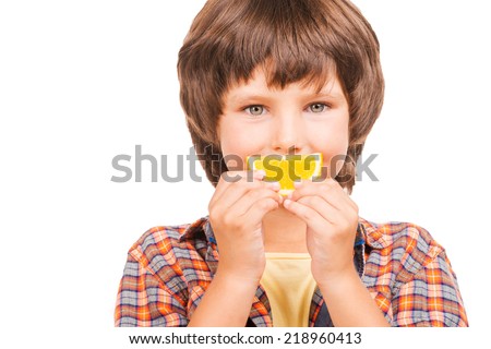 Having fun with orange. Cheerful little boy covering mouth with piece of orange while isolated on white