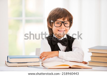 Smart and confident schoolboy. Cute young boy keeping arms crossed while sitting at the table