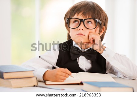 Day dreaming. Bored young boy leaning his face on hand and looking away while sitting at the desk