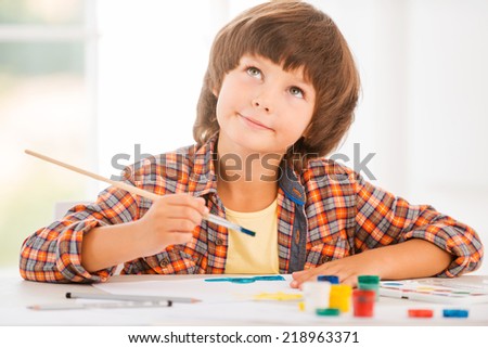 Looking for inspiration. Cute little boy relaxing while painting with watercolors sitting at the table
