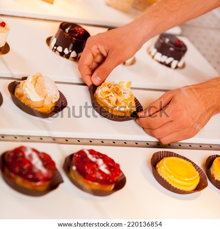 Good choice. Close-up of male hand taking a cupcake from showcase while standing in bakery shop