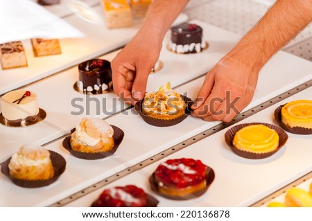 Is this your choice? Close-up of male hand taking a cupcake from showcase while standing in bakery shop