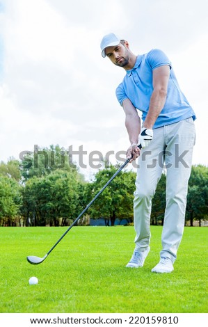Putting green. Full length of young man in sports clothing playing golf while standing on green