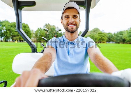 Driving a golf cart. Handsome young man driving a golf cart and looking away