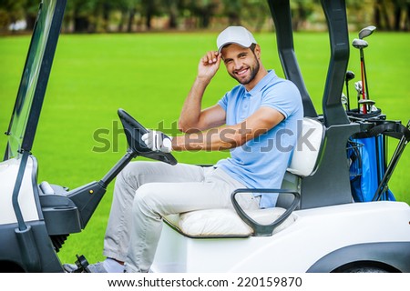 Man driving golf cart. Side view of handsome young man driving a golf cart and looking at camera