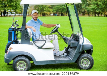 Man driving golf cart. Side view of handsome young man driving a golf cart and looking at camera