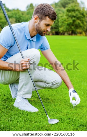 Teeing up. Confident young male golfer placing a golf ball on tee prior