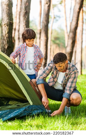 Learning the basics of camping. Cheerful father and son pitching a tent while camping in the forest together