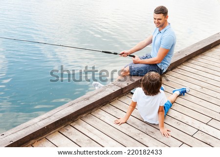 My father is the best in fishing. Top view of cheerful father and son fishing together while sitting at the riverbank