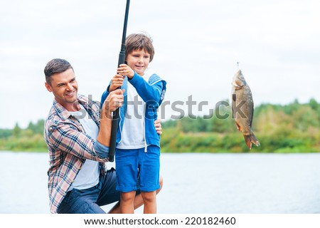 Look what we caught! Father and son stretching a fishing rod with fish on the hook