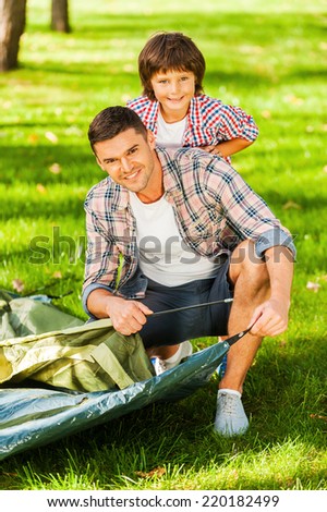 Learning the basics of camping. Cheerful father and son pitching a tent while camping in the forest together