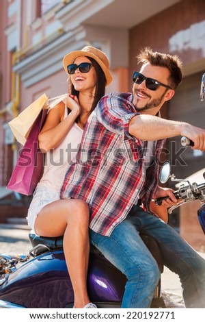 Freedom is in their veins. Side view of beautiful young couple riding scooter together while happy woman carrying shopping bags and bonding