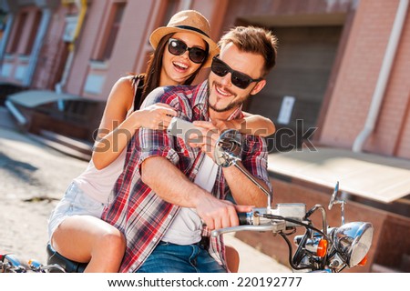 Look at this photo! Beautiful young couple sitting on scooter together while happy woman showing something at her mobile phone