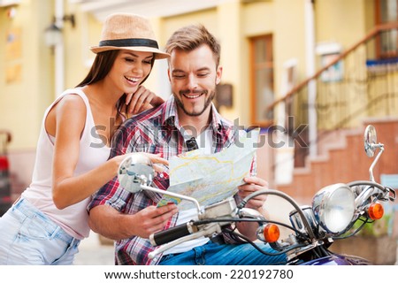Looking for place to go. Beautiful young loving couple sitting on scooter together and examining map while woman pointing it and smiling