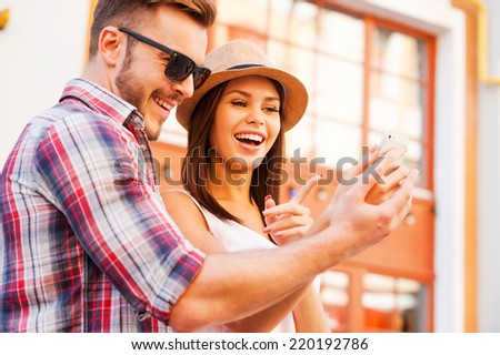 Look at this picture! Happy young loving couple standing outdoors together and looking at the mobile phone