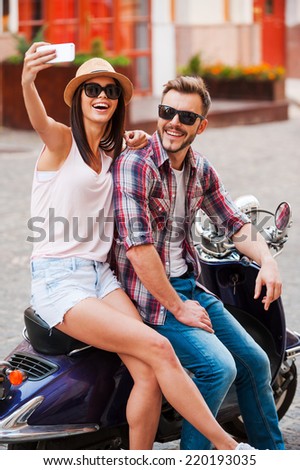 Selfie! Beautiful young loving couple sitting on scooter together and making selfie by their smart phone