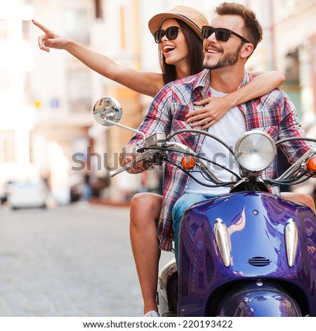 Just look at that! Beautiful young couple riding scooter together while happy woman pointing away and smiling