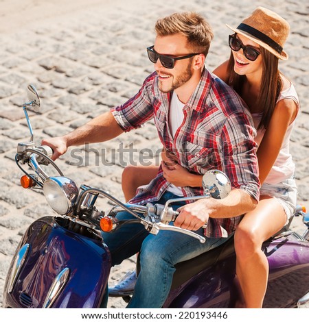 Young and free. Top view of beautiful young couple riding scooter together while happy woman bonding to her boyfriend and smiling