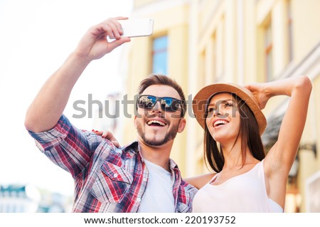 We love making selfies. Low angle view of happy young loving couple making selfie while standing outdoors together