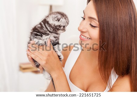 You are so cute! Beautiful young woman holding little kitten in hands and looking at him with smile