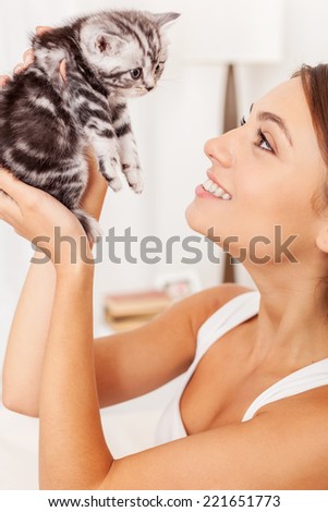 You are so cute! Beautiful young woman holding little kitten in hands and looking at him with smile