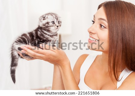 You are so small and cute! Beautiful young woman holding little kitten in hands and looking at him with smile