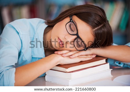 Tired of studying. Tired young women holding her head on the book stack and sleeping while sitting at the library desk
