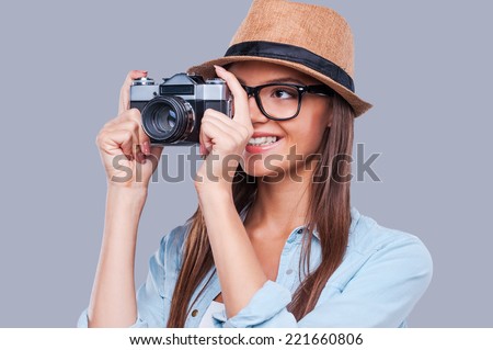 Be creative! Creative young girl taking a photograph and smiling while standing against grey background