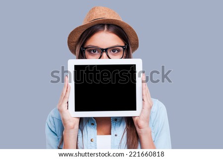 Young woman with her digital tablet. Young women holding her digital tablet in front of her face while standing against grey background