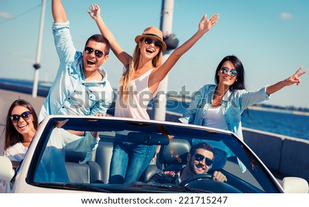 Friends in convertible. Group of young happy people enjoying road trip in their white convertible and raising their arms