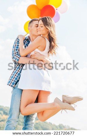 Love is in the air. Man holding a beautiful young woman and balloons while kissing her