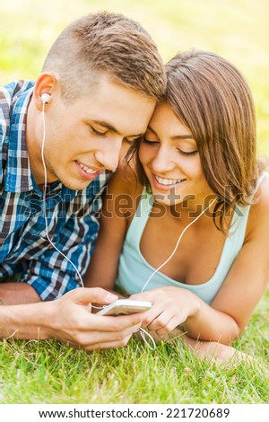 Enjoying music together. Young couple lying on the grass and choosing music on the phone