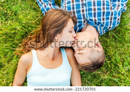 Tender kissing. Top view of a young couple in love lying together on the grass and kissing