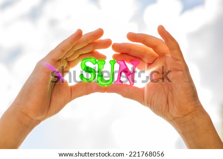 Holding sun in hands. Close-up of sun formed from plastic letters in hands of a child and in front of the sky