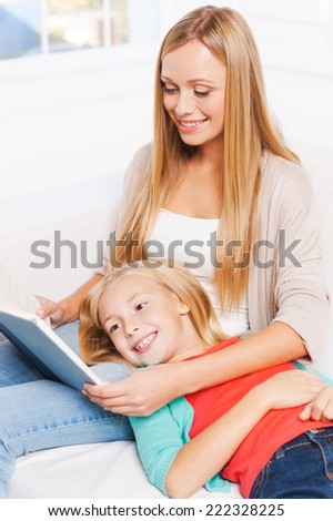 Enjoying their favorite book together. Top view of happy mother and daughter reading together while sitting on the couch at home together