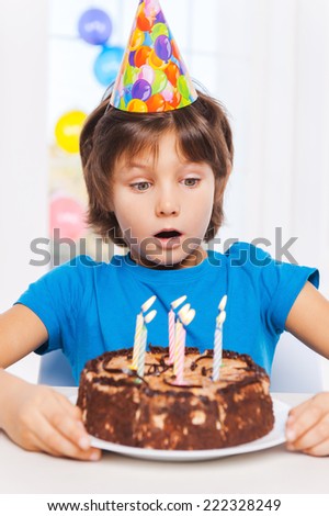 What a surprise! Surprised little boy looking at the birthday cake and preparing to blow the candles